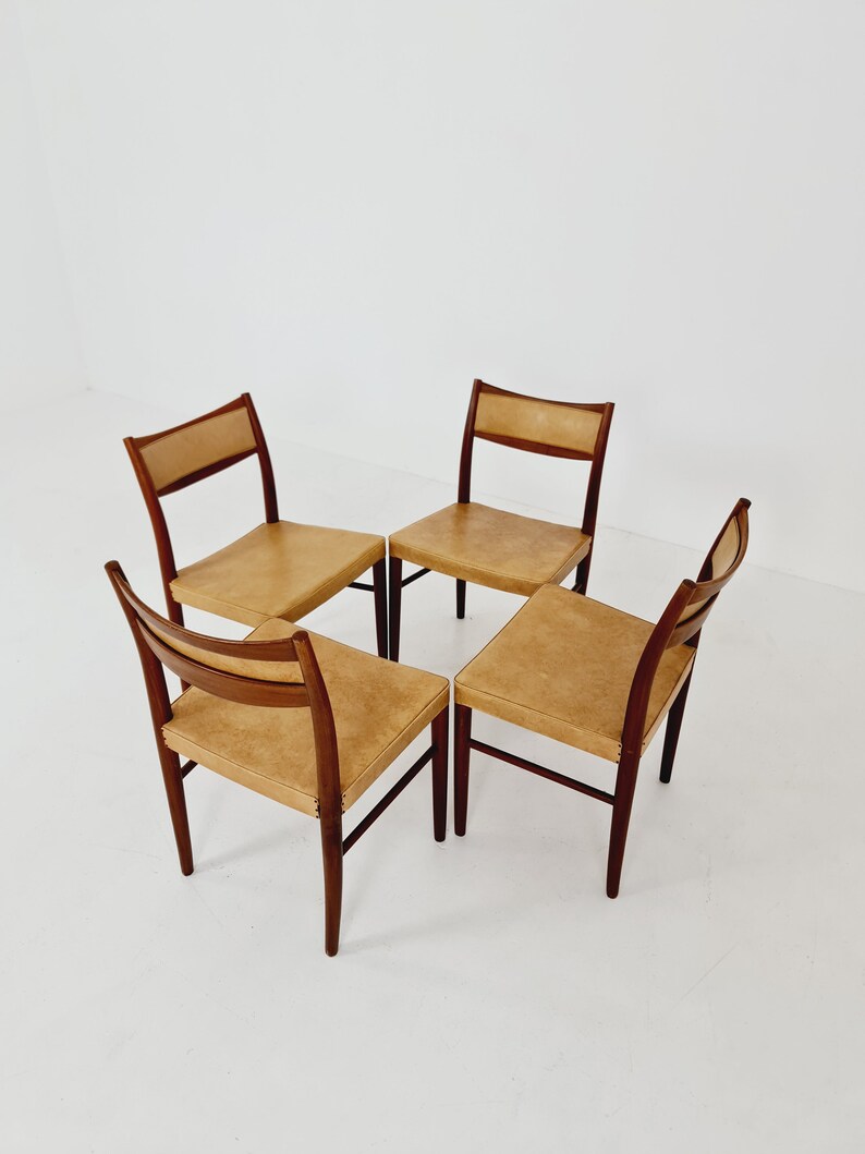 May include: Four mid-century modern dining chairs with a light brown leather upholstery and dark wood frames.