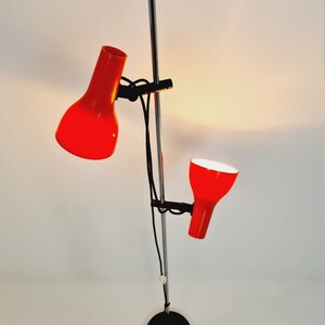 Puede incluir: Una l&aacute;mpara de pie roja y negra con dos pantallas ajustables. La l&aacute;mpara tiene un poste cromado y una base negra.