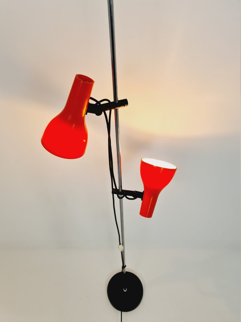 Puede incluir: Una l&aacute;mpara de pie roja y negra con dos pantallas ajustables. La l&aacute;mpara tiene un poste cromado y una base negra.