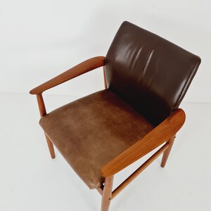 May include: A brown leather armchair with a wooden frame. The chair has a curved back and arms, and the legs are tapered.