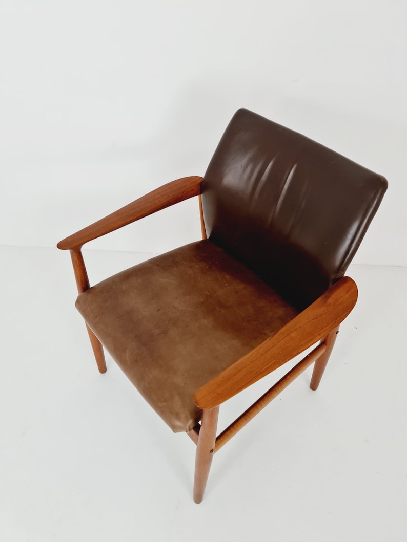 May include: A brown leather armchair with a wooden frame. The chair has a curved back and arms, and the legs are tapered.