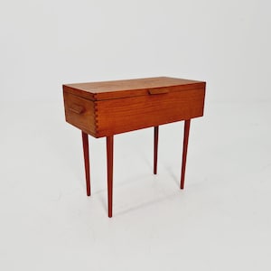 Könnte beinhalten: Ein Beistelltisch aus Holz mit einer Klappplatte und vier schlanken Beinen. Der Tisch ist aus hellbraunem Holz gefertigt und hat ein schlichtes, minimalistisches Design.