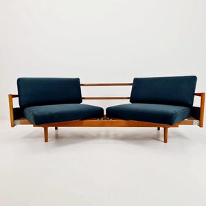 Könnte beinhalten: Ein Zweisitzer-Sofa im Mid-Century-Modern-Stil mit Holzrahmen und marineblauen Kissen. Das Sofa hat ein niedriges Profil mit horizontaler Rückenlehne und Armlehnen. Die Kissen sind rechteckig und aus weichem Stoff.