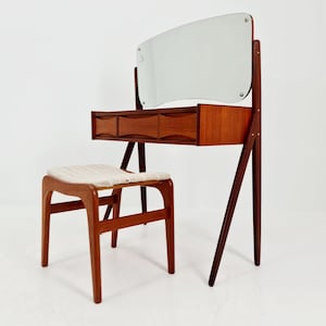 Könnte beinhalten: Ein modernes Schminktisch-Set aus der Mitte des Jahrhunderts mit einem rechteckigen Spiegel, drei Schubladen und einem passenden Hocker. Der Schminktisch und der Hocker sind aus Holz gefertigt und haben einen hellfarbigen Stoffsitz. Der Spiegel ist mit Holzstützen am Schminktisch befestigt.