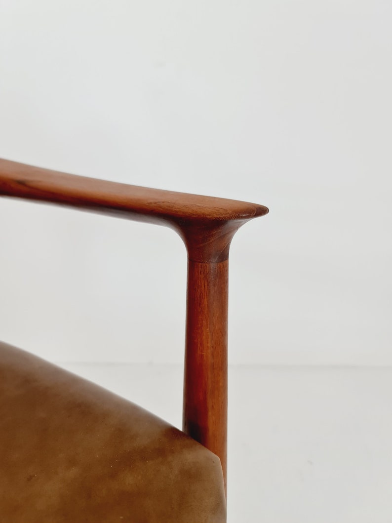 May include: Close-up of the armrest of a brown leather chair with a wooden frame. The armrest is made of solid wood and has a smooth, curved design.