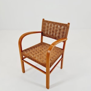 May include: A vintage wooden armchair with a woven seat and backrest. The chair features curved armrests and a light brown finish. The woven material is a darker brown, creating a contrast with the wooden frame. The chair is a classic piece of furniture.
