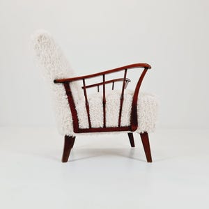 May include: A mid-century modern armchair with a white, fluffy seat and back. The chair features a dark brown wooden frame with curved armrests and a slatted back. The legs are also dark brown.