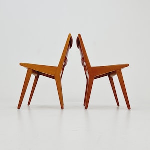 Könnte beinhalten: Zwei Holzstühle im einfachen, modernen Design der Mitte des Jahrhunderts. Die Stühle sind aus hellbraunem Holz gefertigt und haben eine leicht abgewinkelte Rückenlehne.