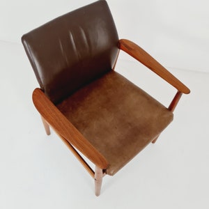 May include: A brown leather armchair with wooden arms and legs. The chair has a simple, mid-century modern design.