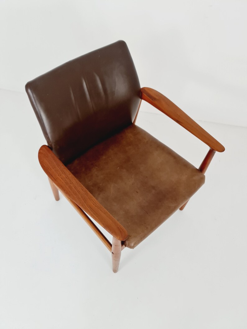 May include: A brown leather armchair with wooden arms and legs. The chair has a simple, mid-century modern design.