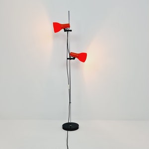 Puede incluir: Una l&aacute;mpara de pie de cromo con dos pantallas rojas ajustables. La l&aacute;mpara tiene una base negra y un cable negro largo.