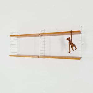 May include: White metal wall-mounted shelving unit with two wooden shelves. The shelves are made of light brown wood. A wooden monkey figurine is hanging from the top shelf.