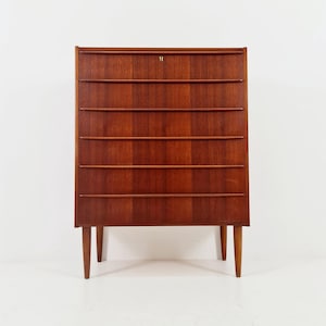 May include: A mid-century modern wooden cabinet with six drawers and a top compartment. The cabinet is made of a reddish-brown wood and has a keyhole on the top. It stands on four tapered legs.