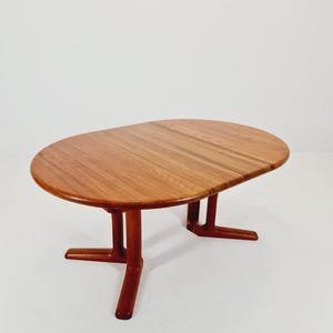 Op de afbeelding: Een ovale eettafel in mid-century modern stijl van hout. De tafel heeft een warme bruine afwerking en een uniek potenontwerp. De tafel is ongeveer 152 cm lang en 102 cm breed.