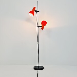 Puede incluir: Una l&aacute;mpara de pie cromada con dos pantallas de l&aacute;mpara naranja ajustables. La l&aacute;mpara tiene una base negra y un cable negro largo.