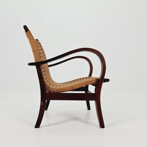 May include: A vintage wooden armchair with a woven seat and backrest. The chair has a dark brown frame with curved armrests and legs. The seat and back are made of a light brown woven material, creating a contrast with the dark wood.
