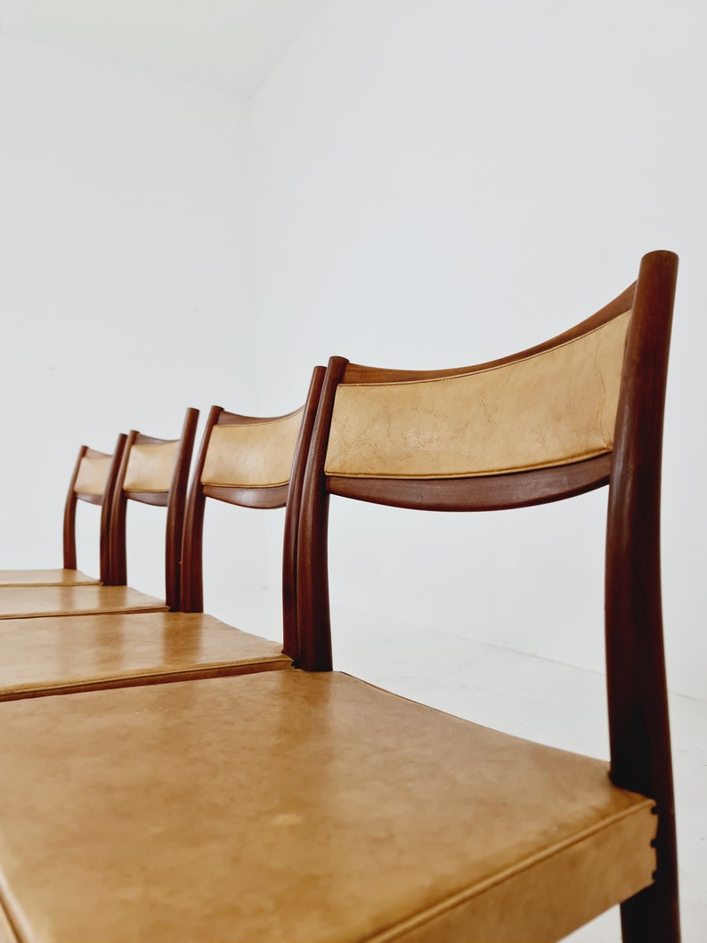 May include: Four brown wooden chairs with tan leather seats. The chairs are lined up in a row.