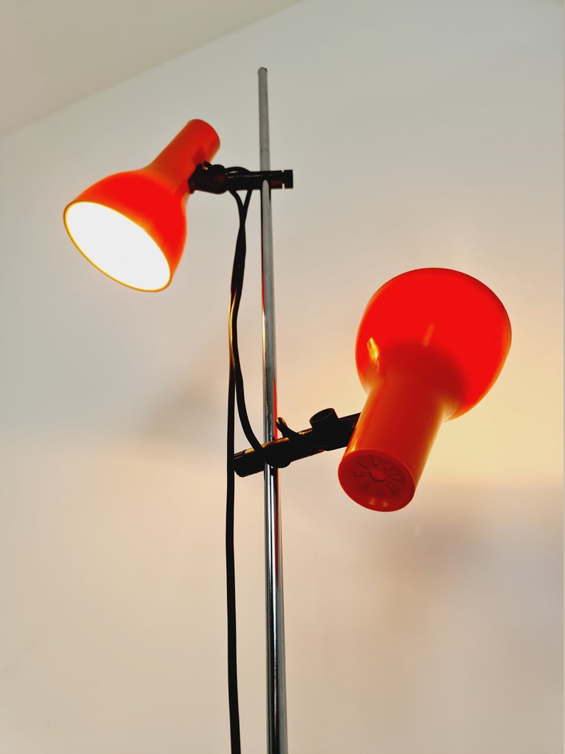 Puede incluir: Una l&aacute;mpara de pie de cromo con dos pantallas de l&aacute;mpara naranja ajustables. Las pantallas de l&aacute;mpara est&aacute;n sujetas al poste con abrazaderas negras.