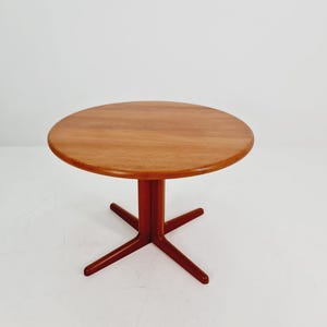 Könnte beinhalten: Ein runder Beistelltisch aus Holz mit warmem, rötlich-braunem Finish. Die Tischplatte hat einen Durchmesser von ca. 61 cm und wird von einem Mittelfuß mit vier abgewinkelten Beinen getragen. Der Tisch hat ein modernes Design aus der Mitte des Jahrhunderts.