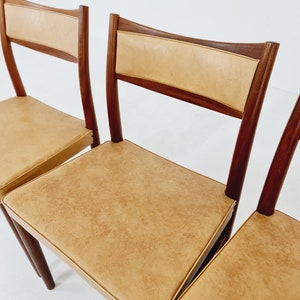 May include: Four mid-century modern dining chairs with a light brown leather upholstery and dark wood frames.