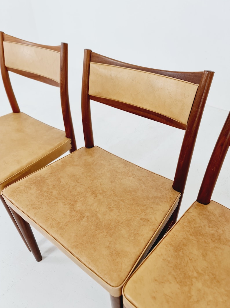 May include: Four mid-century modern dining chairs with a light brown leather upholstery and dark wood frames.