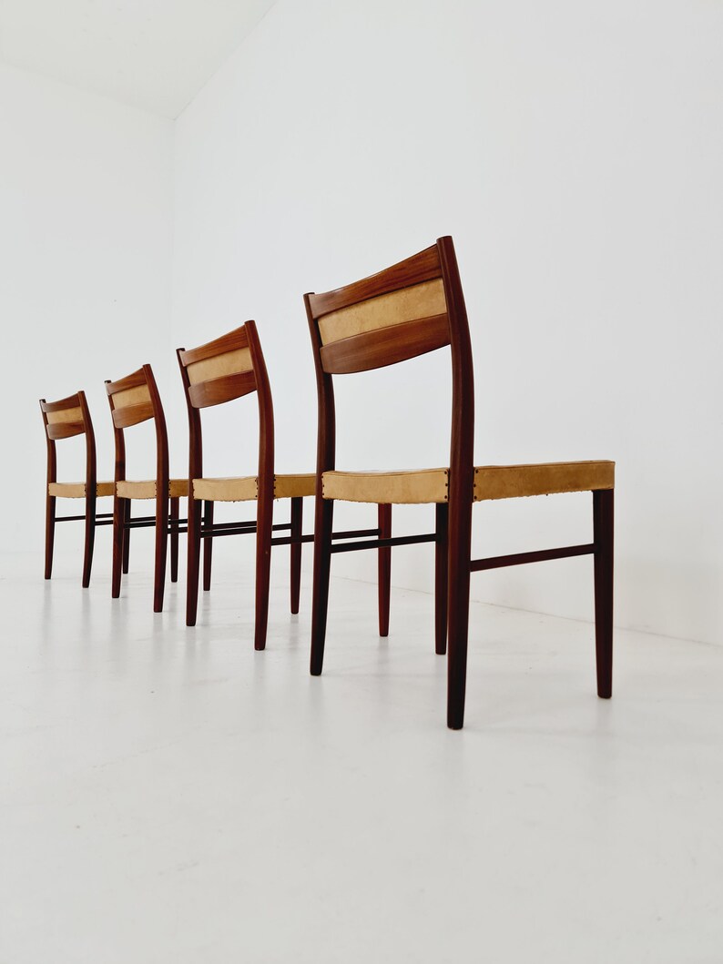 May include: Four wooden chairs with light brown upholstery and dark brown legs. The chairs are arranged in a row, facing the same direction.