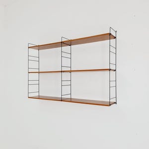 May include: A wall-mounted shelving unit with three wooden shelves and a black metal frame. The shelves are a warm brown color, and the frame has a minimalist design. The unit is mounted on a white wall.