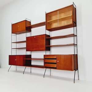 Könnte beinhalten: Mid-Century Modern Wandregal mit einer Kombination aus offenen Regalen, Schränken und Schubladen. Das Regal hat eine warme Holzoberfläche, schwarze Metallstützen und einen Schrank mit Glasfront. Eine stilvolle Aufbewahrungslösung.