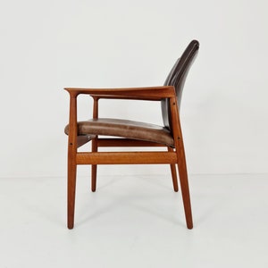 May include: A brown leather chair with a wooden frame. The chair has a high back and arms. The chair is sitting on a white surface.