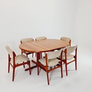 Könnte beinhalten: Ein Esszimmer-Set im Mid-Century-Modern-Stil mit einem ovalen Holztisch und sechs passenden Stühlen. Der Tisch hat eine warme Holzoberfläche, und die Stühle haben hell gepolsterte Sitze und Rückenlehnen. Das Set ist für ein Esszimmer konzipiert.