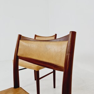 May include: Two mid-century modern dining chairs with brown wood frames and tan leather upholstery.