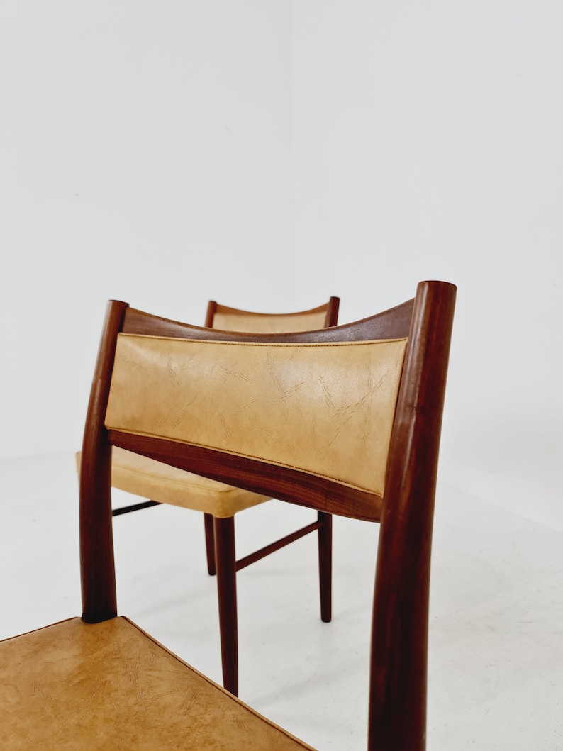 May include: Two mid-century modern dining chairs with brown wood frames and tan leather upholstery.