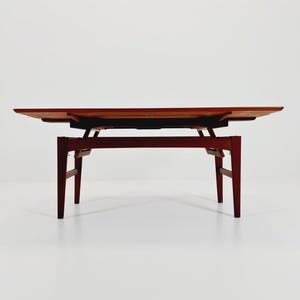 May include: A mid-century modern coffee table with a rectangular top and a dark wood finish. The table has a unique design with a lower shelf and angled legs. The table is approximately 48 inches long, 20 inches wide, and 16 inches high.