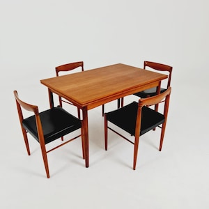 May include: A rectangular wooden dining table with a warm brown grain finish, accompanied by four matching chairs. Each chair features a curved wooden backrest and a seat upholstered in smooth black material, supported by four tapered legs.