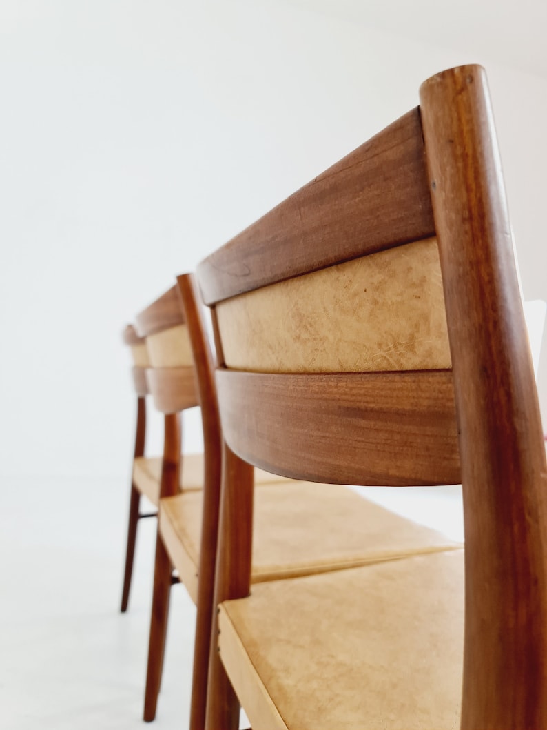 May include: Four wooden chairs with light brown upholstery and a dark brown wood frame. The chairs are arranged in a row, with the back of the chair in the foreground.