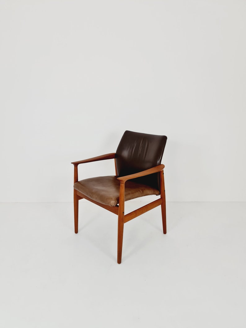 May include: A brown leather armchair with a wooden frame. The chair has a high back and arms, and the seat is slightly angled.