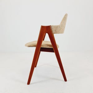 Könnte beinhalten: Ein Stuhl im Mid-Century-Modern-Stil mit Holzrahmen und Sitzfläche und Rückenlehne aus gewebtem Stoff. Der Stuhl hat eine geschwungene Rückenlehne und Armlehnen, und die Beine sind angewinkelt. Das Holz hat eine warme braune Farbe, und der Stoff ist ein neutrales Beige.