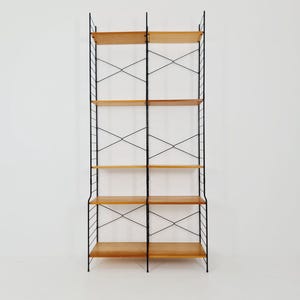 Op de afbeelding: Een hoge, moderne boekenplank uit het midden van de eeuw met vijf houten planken. De planken worden ondersteund door een zwart metalen frame met een X-vormig ontwerp. De unit staat tegen een witte achtergrond.