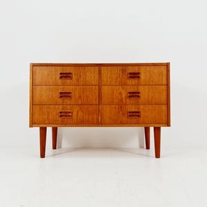 May include: A mid-century modern dresser with six drawers. The dresser is made of wood with a warm, reddish-brown finish. It has a rectangular shape with four tapered legs. Each drawer has a recessed handle. The dresser is approximately 30 inches wide.