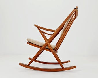 May include: A wooden rocking chair with a light-colored cushion and a natural wood finish. The chair has a slatted back and armrests, and the seat is upholstered in a neutral fabric. The chair is designed with a mid-century modern aesthetic.