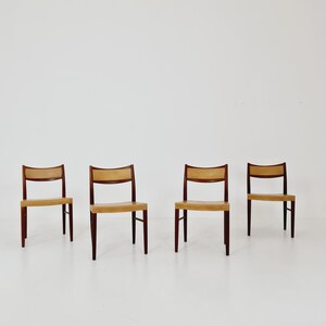 May include: Four chairs with a light brown leather seat and dark wood legs. The chairs are arranged in a row on a white floor.