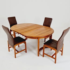 Peut inclure: Un ensemble de salle à manger composé d'une table ovale en bois au grain brun clair et de quatre chaises avec des cadres en bois et un revêtement en cuir brun foncé sur les sièges et les dossiers hauts. La table a une base centrale.