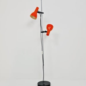 Puede incluir: Una l&aacute;mpara de pie de cromo con dos pantallas ajustables de color naranja. La l&aacute;mpara tiene una base negra y un cable largo.