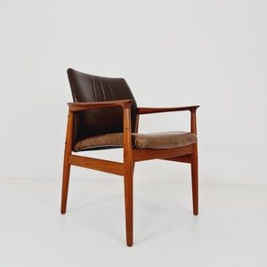 May include: A brown leather armchair with a wooden frame. The chair has a curved back and a slightly angled seat. The chair is sitting on a white background.