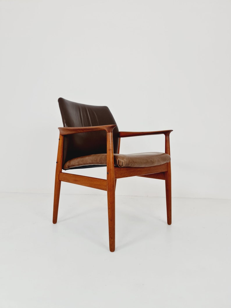 May include: A brown leather armchair with a wooden frame. The chair has a curved back and a slightly angled seat. The chair is sitting on a white background.