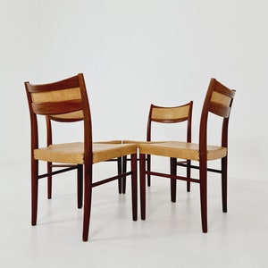 May include: Four wooden chairs with tan leather seats. The chairs are arranged in a square formation, with the backs of the chairs facing the camera.