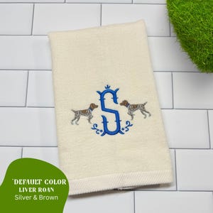 May include: Cream-colored hand towel with an embroidered blue letter "S" and two dog illustrations. The dogs are brown and white. The towel has a textured appearance. The text "DEFAULT COLOR LIVER ROAN Silver & Brown" is in the lower left corner.