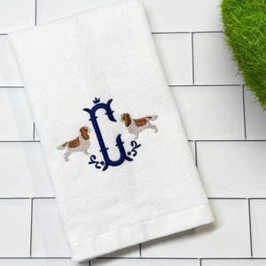 May include: White hand towel with an embroidered navy blue letter "C" and two Cavalier King Charles Spaniel dog designs. The towel is made of a soft, absorbent material, perfect for use in a bathroom or kitchen.