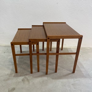 Puede incluir: Un conjunto de tres mesas nido de madera. Las mesas son todas de la misma forma y tamaño, pero tienen diferentes alturas. Las mesas son de color marrón claro y tienen un acabado liso.