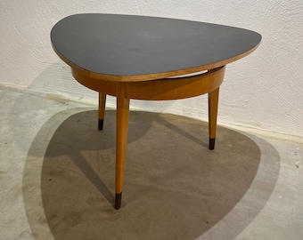 May include: A triangular wooden side table with a black top and tapered legs. The table has a unique design with a curved edge on the underside of the top.